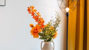 A white table with a vase of orange flowers and a geometric floor lamp.