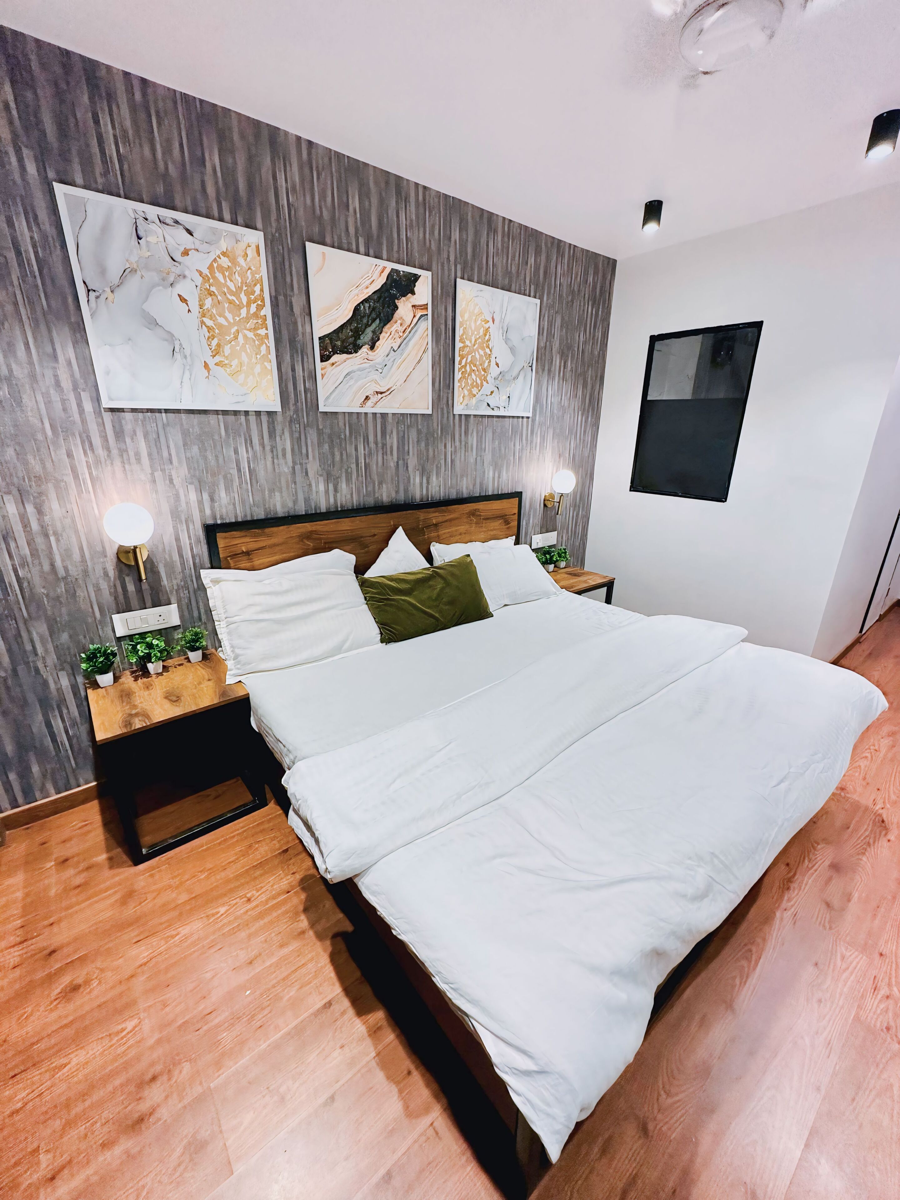 A modern bedroom with a large bed, wooden headboard, and three abstract wall art pieces.