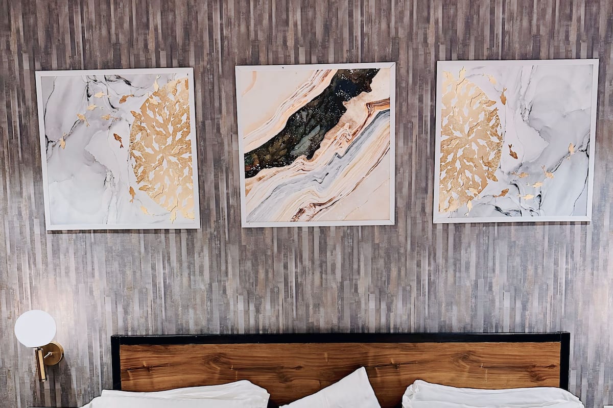 Ein Schlafzimmer mit einem Holz-Kopfteil, weißer Bettwäsche und drei abstrakten Bildern an der Wand.