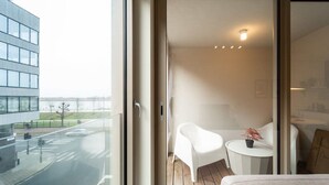 A modern interior with a glass door leading to a balcony. Inside, there is a white chair, a small round table with a potted plant, and a sofa. - Wonderful 1BR apartment in Antwerp (Antwerpen)
