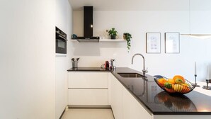 A modern kitchen with white cabinetry, a black countertop, a stainless steel sink, and a fruit bowl. - Wonderful 1BR apartment in Antwerp (Antwerpen)