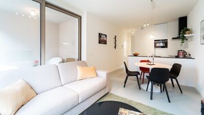 A modern living room with a sofa, a dining table with chairs, a kitchen area, and a large window. - Wonderful 1BR apartment in Antwerp (Antwerpen)