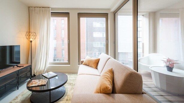 A modern living room with a sofa, a coffee table, a TV, and a large window. - Wonderful 1BR apartment in Antwerp (Antwerpen)