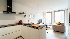 Una cocina moderna con armarios blancos, encimera negra y estufa integrada. Hay un área de comedor con sofá y una mesa de centro.