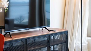 Una sala de estar moderna con una televisión de pantalla plana sobre un mueble de madera, una mesa redonda y una lámpara de pie.