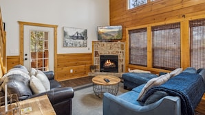 A cozy living room with a fireplace, wooden walls, and a television. - 3 BR (11 Guests) near Parkway - WiFi, Hot Tub, Fire Pit, Game Room, Free Tickets (Sevierville)