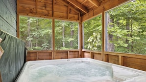 A hot tub in a wooden cabin with large windows overlooking a forest. - 3 BR (11 Guests) near Parkway - WiFi, Hot Tub, Fire Pit, Game Room, Free Tickets (Sevierville)