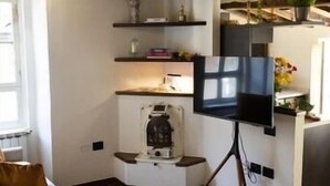 Un salon avec un téléviseur posé sur un meuble, des poutres en bois au plafond, un canapé et une machine à café.