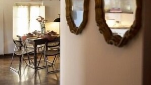 Un intérieur rustique avec des poutres apparentes, un coin repas comprenant des chaises et une table, et deux miroirs décoratifs accrochés au mur.