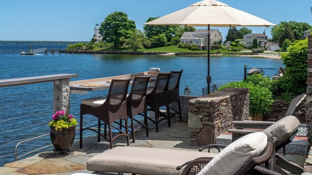 Un patio con mesa y sillas, con vista a un lago y casas al fondo.