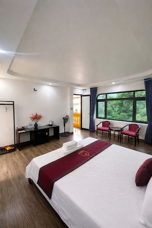 A hotel room with a large bed, a desk, two chairs, a fan, and a view of greenery outside. - La Mai Tam Coc Homestay (Hoa Lu)