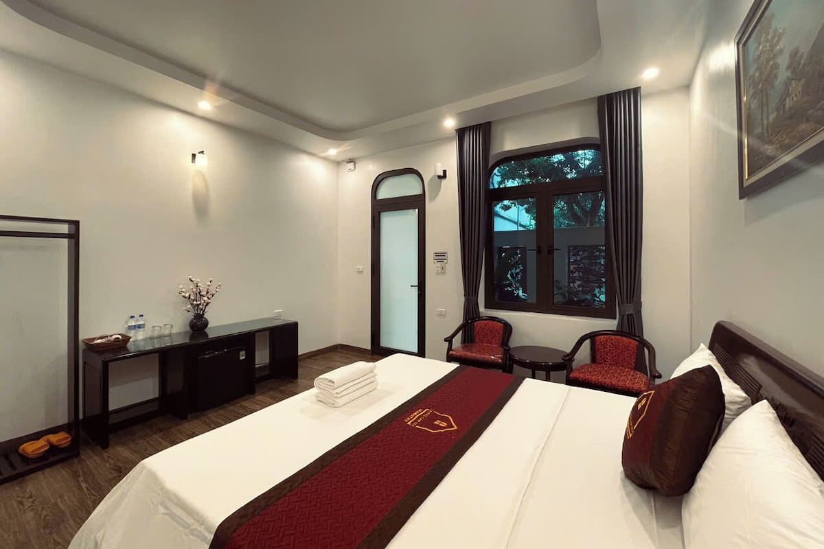Quarto de hotel com uma cama grande, uma escrivaninha, uma cadeira e uma janela com vista para árvores.
