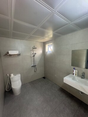 Een moderne badkamer met douche, toilet, wastafel en een klein raam.