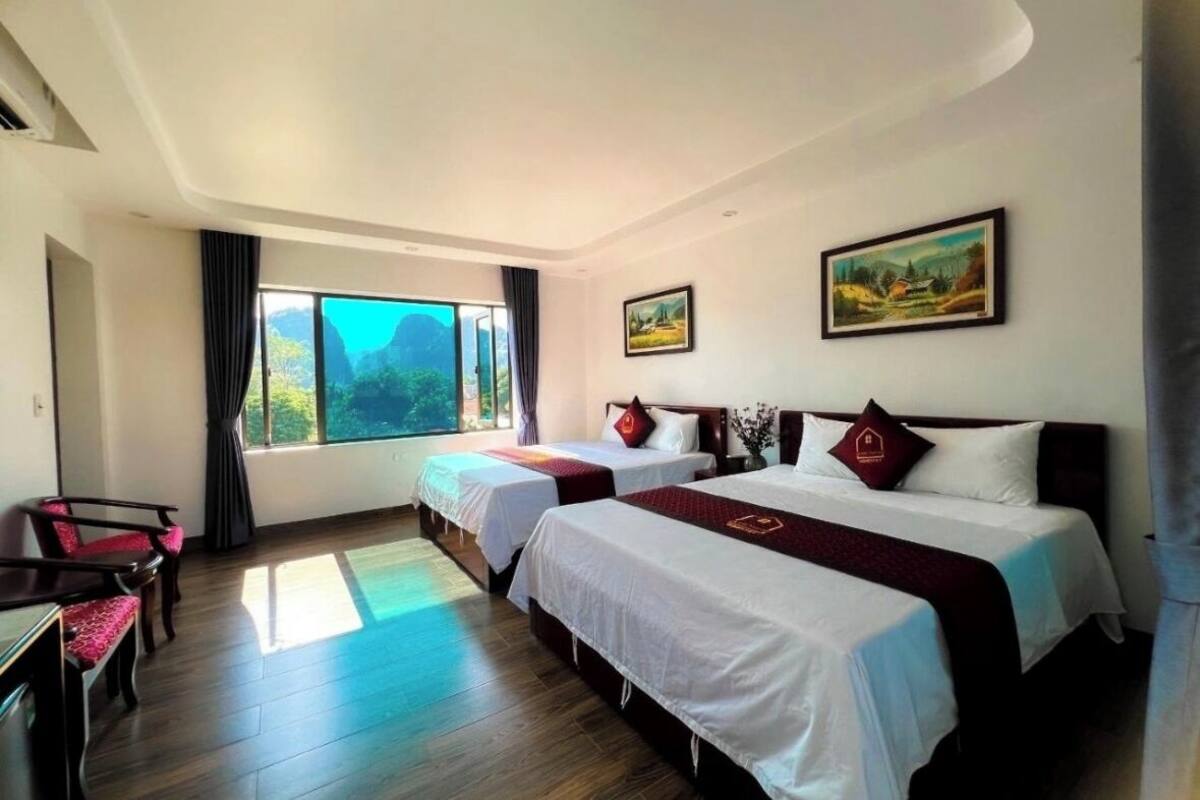 Quarto de hotel com duas camas, uma escrivaninha, cadeiras e janelas amplas com vista.