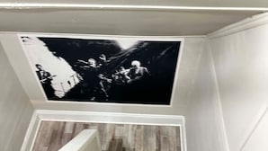 Una escalera con acabado gris oscuro y adornos blancos que conduce a un rellano con una fotografía blanco y negro de una banda tocando.
