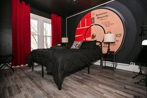 Ein Schlafzimmer mit einem schwarzen Bett, roten Vorhängen, einer Wanduhr und einer Lampe.