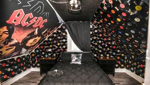 Un dormitorio con una cama, un cartel y una pared repleta de discos de vinilo.