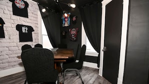 Une pièce avec un mur en briques, des rideaux noirs, une table en bois et des chaises noires.