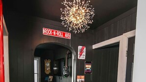 Un couloir aux murs sombres, avec un plancher en bois et un lustre. On y voit une enseigne indiquant « BROCK-N-ROLL AVE » et une porte sur la droite.