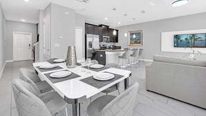 A modern kitchen with dark cabinets, a central island, and a dining area with a white table and grey chairs. - Marvel | Mickey | Splash Pool | 4 Miles Disney 4876 (Kissimmee)