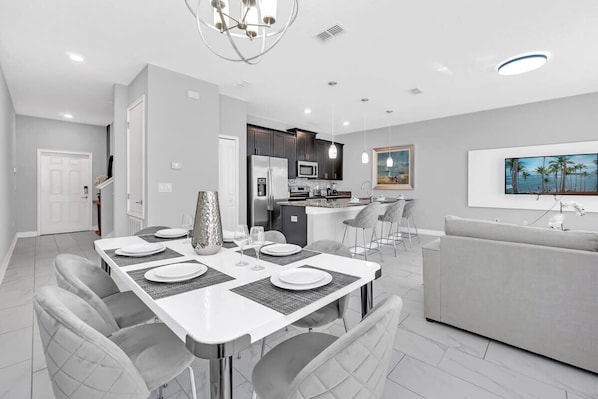 A modern kitchen with dark cabinets, a central island, and a dining area with a white table and grey chairs. - Marvel | Mickey | Splash Pool | 4 Miles Disney 4876 (Kissimmee)