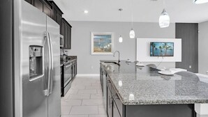 A modern kitchen with a stainless steel refrigerator, a granite countertop island, and pendant lighting. - Marvel | Mickey | Splash Pool | 4 Miles Disney 4876 (Kissimmee)