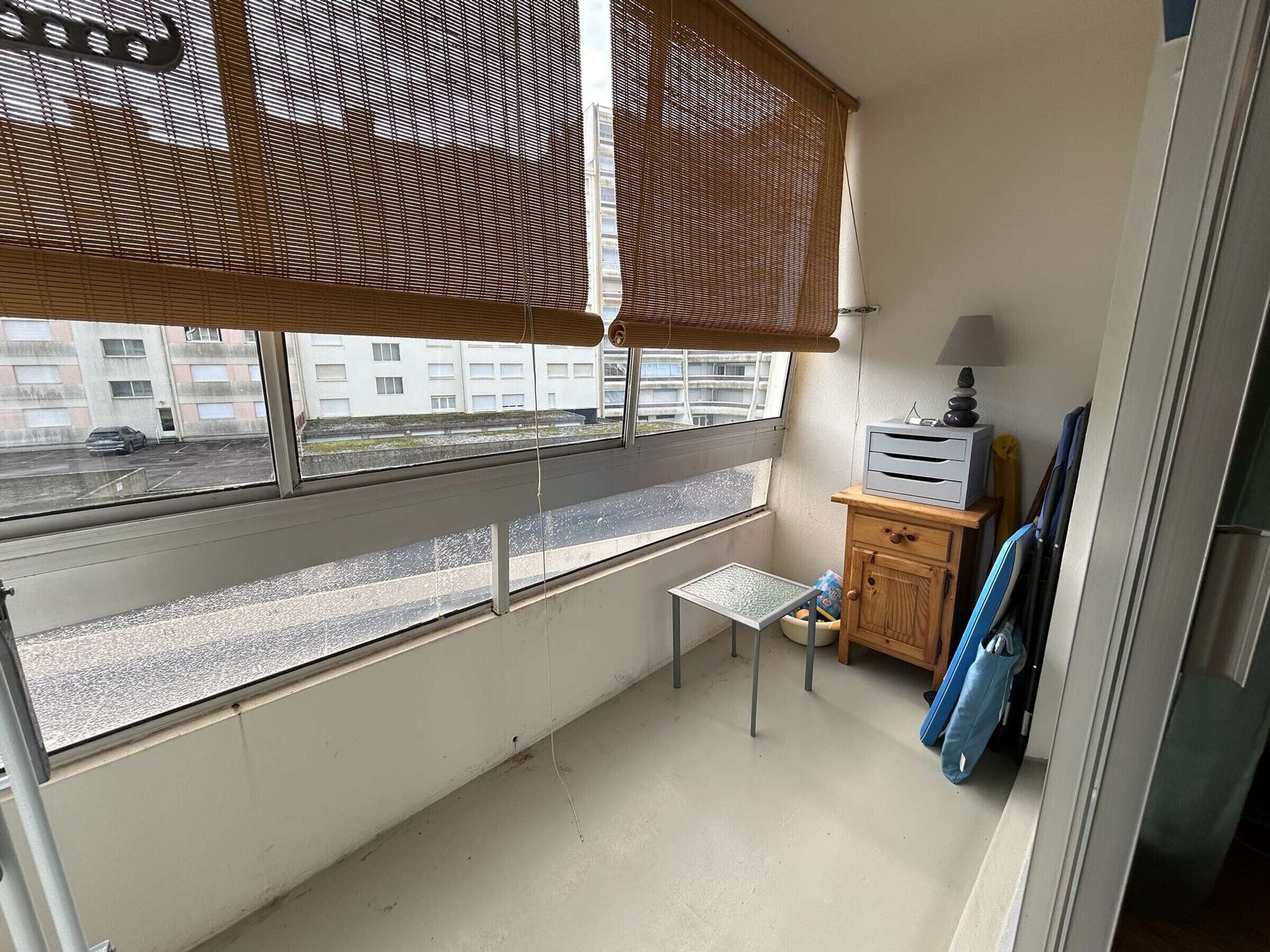 Ein kleiner Balkon mit Blick auf einen Parkplatz und Gebäude, ein kleiner Tisch und ein Holzschrank mit einer Lampe.