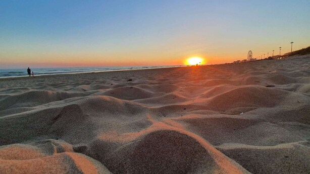 A beach with sand dunes and a sunset in the background.