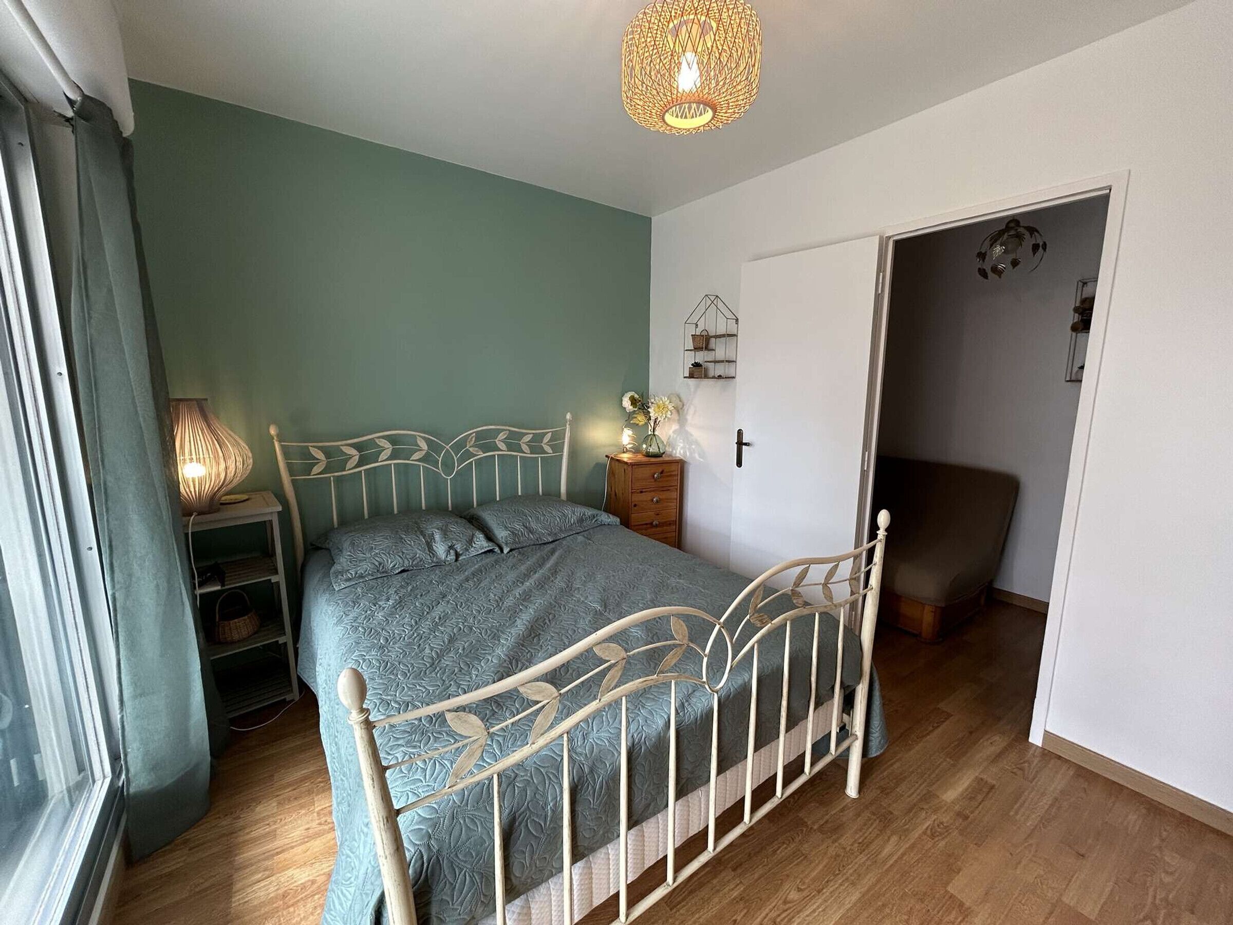 Un dormitorio con cama, mesita de noche, lámpara y una puerta que da a otra habitación.