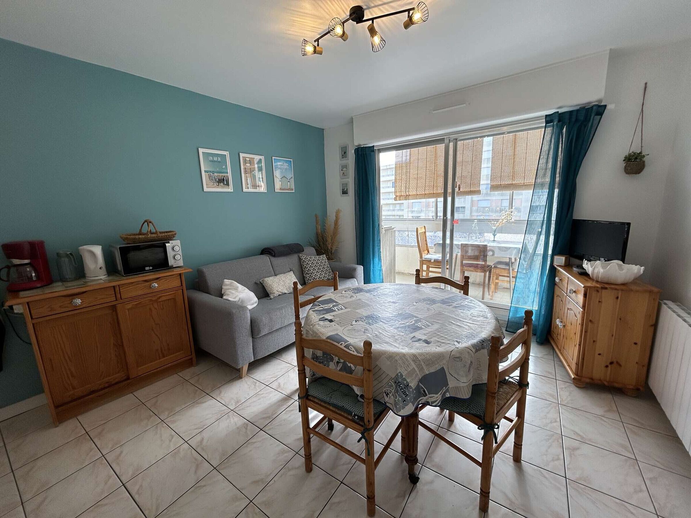 Uma sala de estar aconchegante com um sofá, uma mesa de jantar com cadeiras, uma TV e uma área de cozinha com micro-ondas e cafeteira.