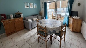 A cozy living room with a sofa, a dining table with chairs, a TV, and a kitchen area with a microwave and coffee maker.