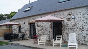 A stone building with a patio area featuring outdoor seating and umbrellas. - Charming cottage on hillside - Private garden, parking (Canville-la-Rocque)