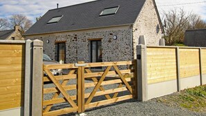 A stone building with a sloped roof, a wooden gate, and a car parked inside. - Charming cottage on hillside - Private garden, parking (Canville-la-Rocque)