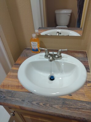 A bathroom sink with a wooden countertop, a mirror above it, and a bottle of hand soap.