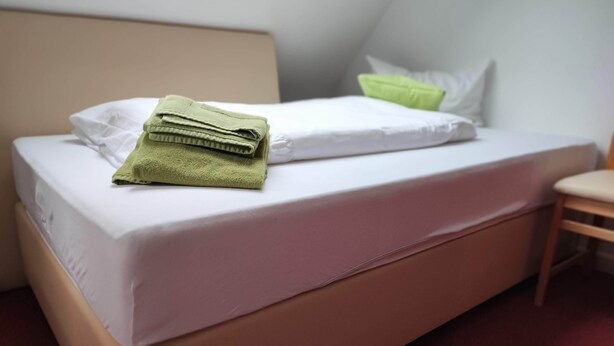 A single bed with a white mattress and a green towel folded on top. - Room in Guest Room - Single Room With Shared Bathroom and Kitchen (Forbach)