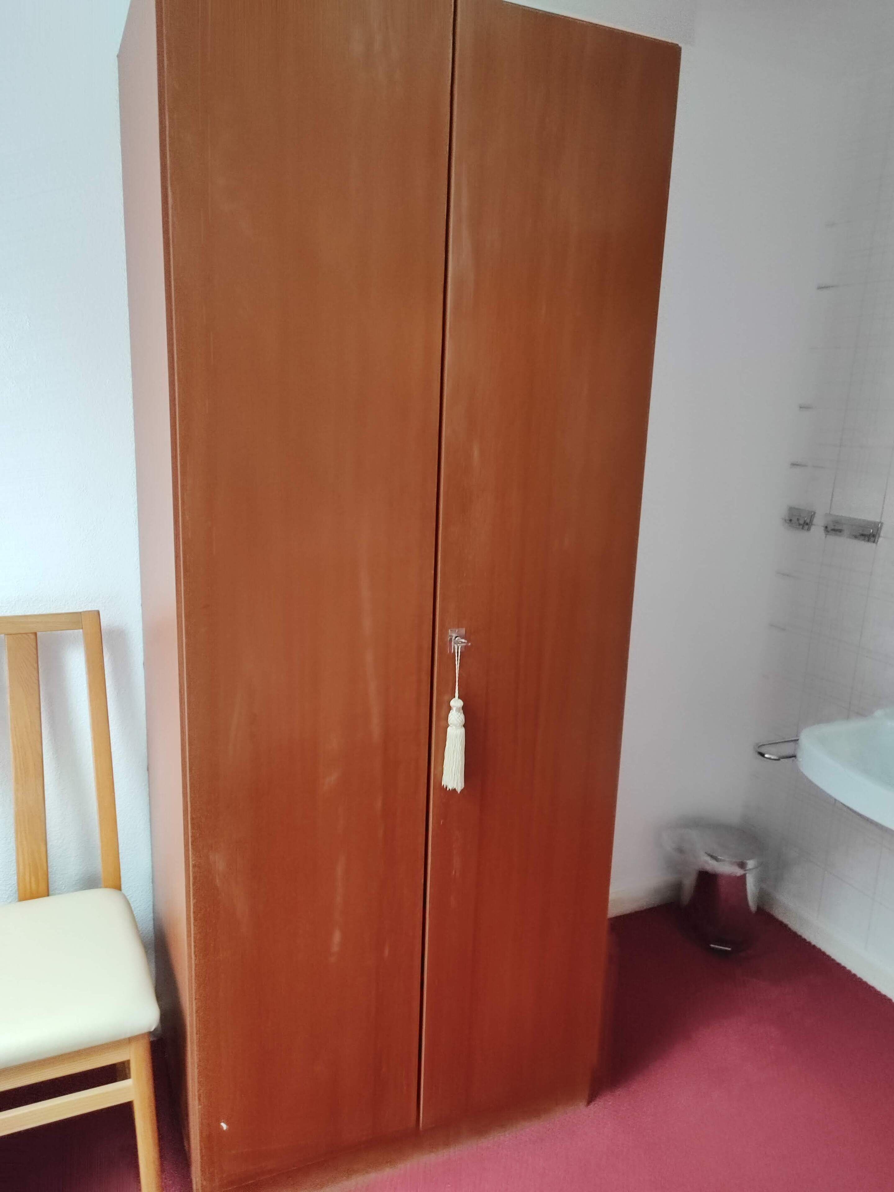 Une armoire en bois avec une poignée blanche, une chaise en bois et un lavabo blanc dans une salle de bain.