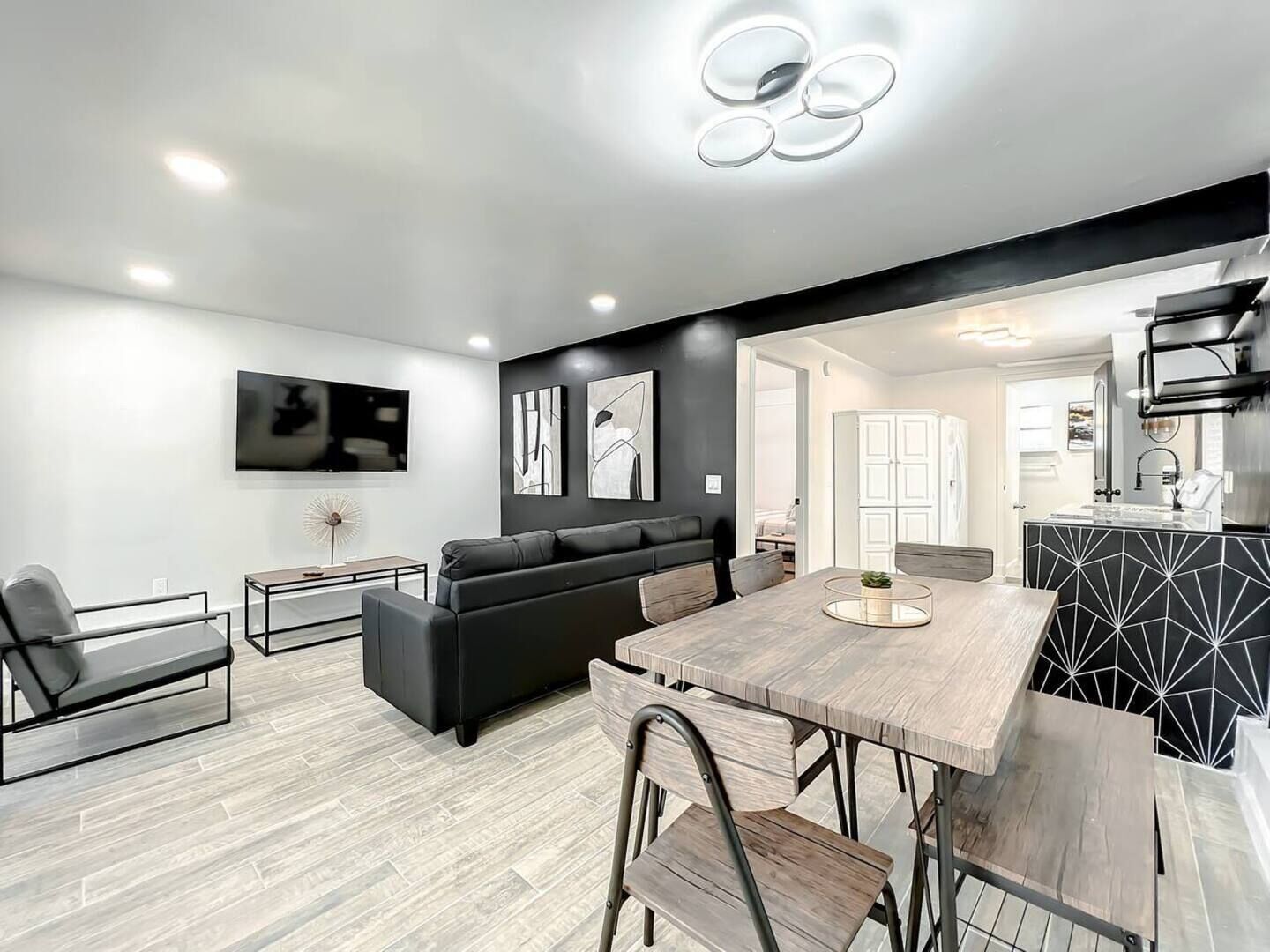 A modern living room with a black sofa, a dining table, and a TV mounted on the wall.