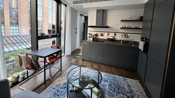 Una cocina moderna con una isla grande, un comedor con mesa y sillas, y vistas de la ciudad a través de amplios ventanales.