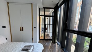 Un dormitorio moderno con una cama grande, un armario y vistas a la ciudad a través de amplios ventanales.