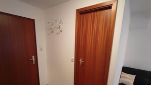 A hallway with two wooden doors, a light switch, and a wall-mounted light fixture. - Room in Guest Room - Pension Forelle - Suite (Forbach)