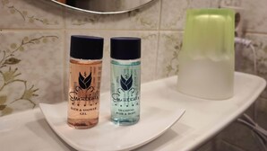 Two bottles of Essentials bath and shower gel and shampoo hair and body on a white tray in a bathroom with a mirror and patterned tiles. - Room in Guest Room - Pension Forelle - Suite (Forbach)