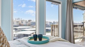 Un dormitorio con un ventanal grande, una cama con una manta blanca y una bandeja con dos tazas.