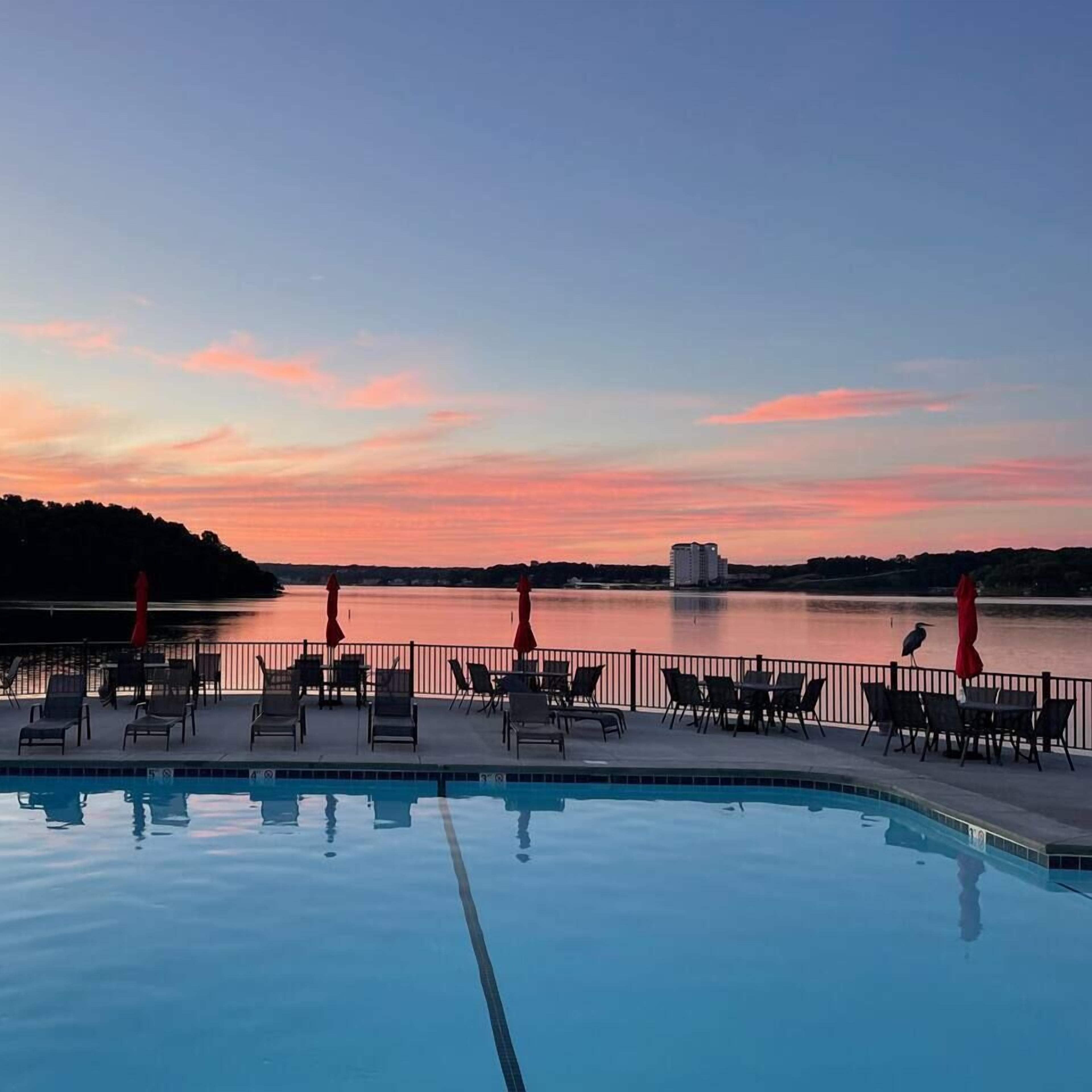 A poolside area with lounge chairs and umbrellas, overlooking a body of water during sunset.