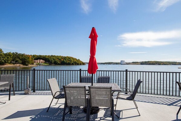A deck with outdoor furniture, a red umbrella, and a view of a lake with a distant shoreline.