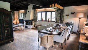 Un salon chaleureux avec une cheminée, un coin repas avec une longue table et des chaises, et un téléviseur.