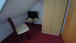 A small room with a single chair, a table with a television, and a wardrobe. - Room in Guest Room - Single Room With Shared Bathroom and Kitchen (Forbach)