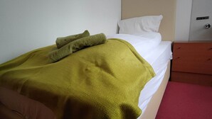 A bed with a green blanket, white pillows, and a wooden nightstand with drawers. - Room in Guest Room - Single Room With Shared Bathroom and Kitchen (Forbach)