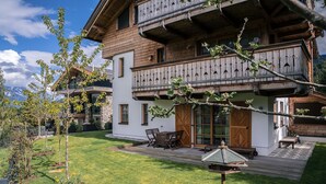 Una cabaña de madera con balcón, un patio con mobiliario exterior y un jardín bien cuidado.