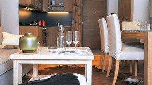 Una cocina moderna con armarios de madera, un comedor con sillas blancas y una mesa dispuesta con vasos y un jarrón.