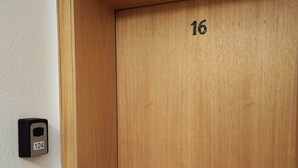 Puinen ovi, jonka numeronumero on 16, ovipuhelin ja valokytkin seinässä.